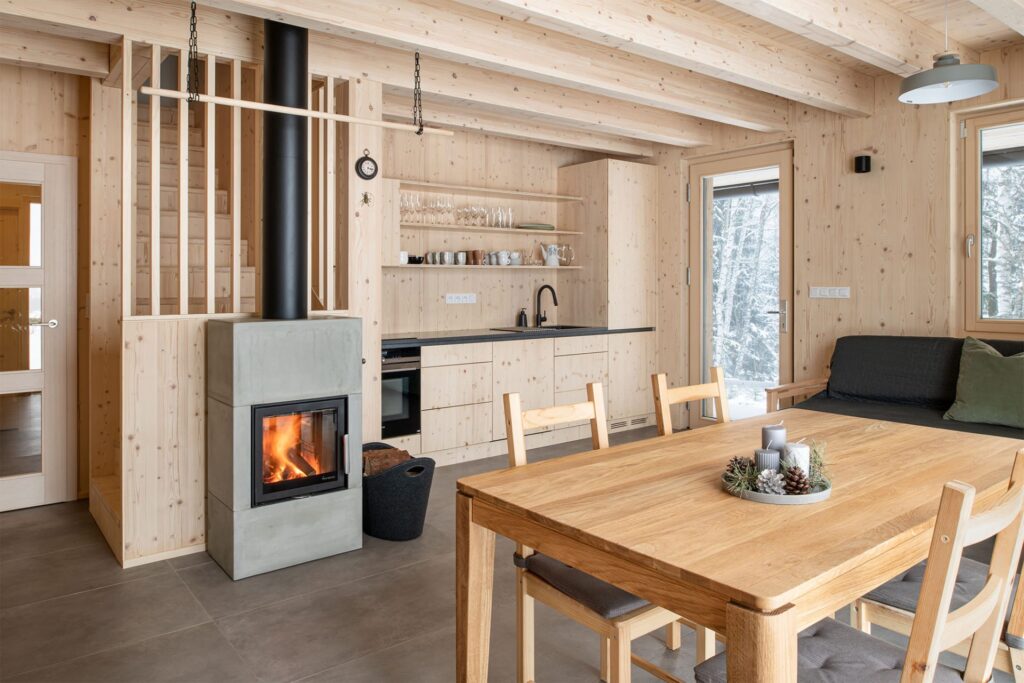 Obývací prostor s kuchyní, jídelním stolem a krbovými kamny v dřevostavbě