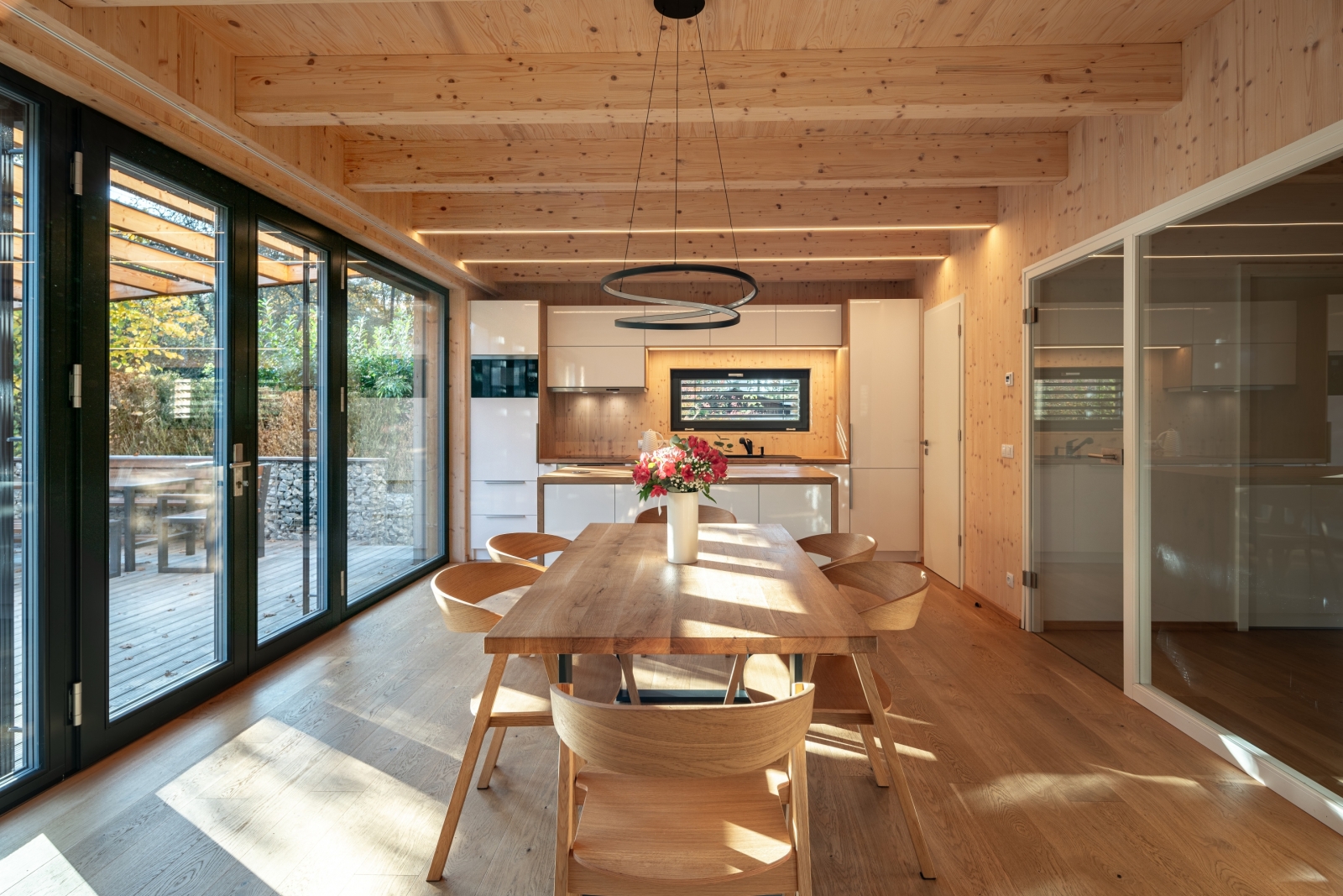 Jídelna v dřevostavbě s dřevěným stropem, skleněnými dveřmi a velkým stolem
