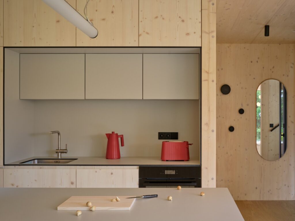Vestavěná kuchyně v interiéru s přiznanými CLT panely a červenými doplňky