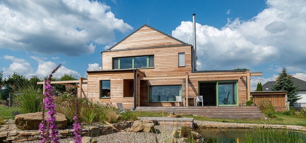 Moderní dřevostavba s dřevěnou fasádou, terasou a jezírkem v zahradě