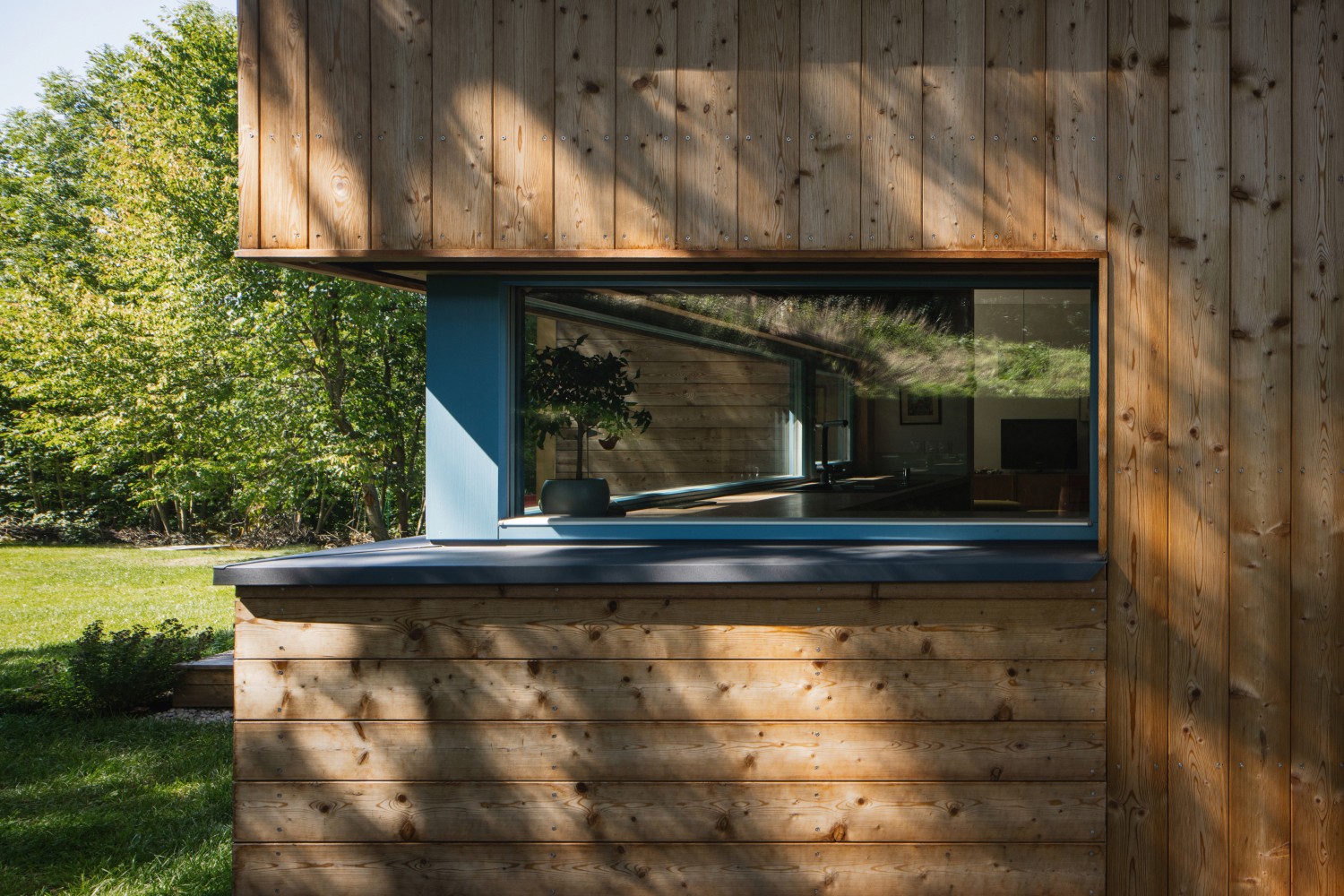 Dřevěná fasáda s oknem a modrým ostěním u moderní dřevostavby z CLT panelů