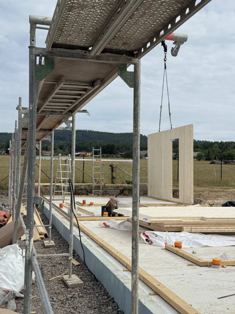 Jeřábová montáž masivního CLT stěnového panelu na základovou desku při výstavbě projektu Za lány.