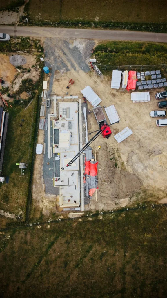 Letecký pohled na staveniště projektu Za lány během montáže CLT panelů s jeřábem a připravenými konstrukčními díly.