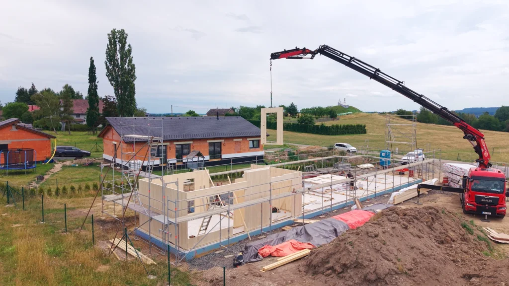Jeřábové osazování stěnového CLT panelu s okenním otvorem při výstavbě projektu Za lány.
