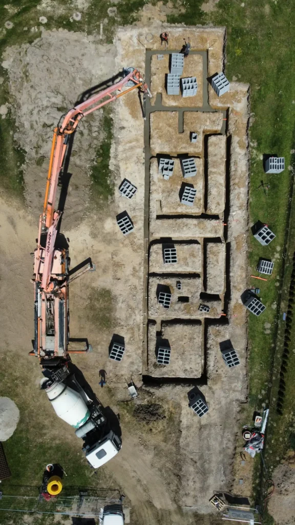 Letecký pohled z dronu na betonáž základových pasů s autodomíchávačem a čerpadlem betonu v Zalánech.