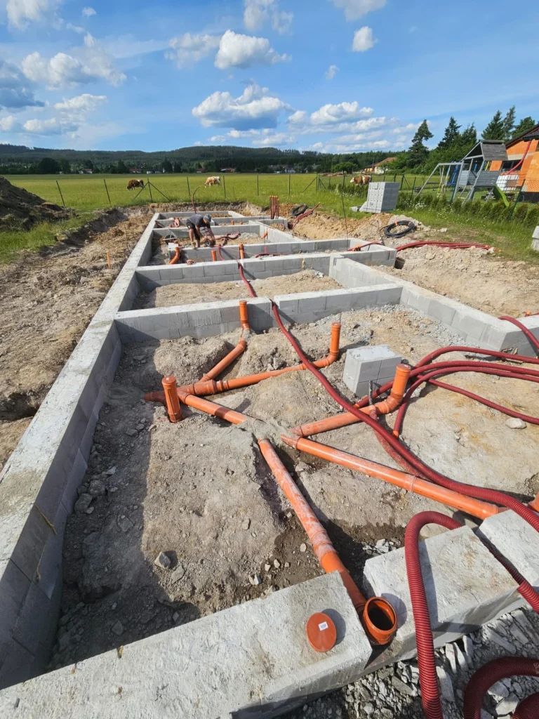 Prostupy a červené chráničky pro inženýrské sítě vyvedené v základech domu na staveništi v Zalánech.
